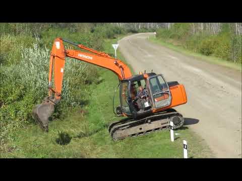 Видео: Гусеничный экскаватор Хитачи выкапывает заросли кустарников мешающих обзору на пересечении дорог